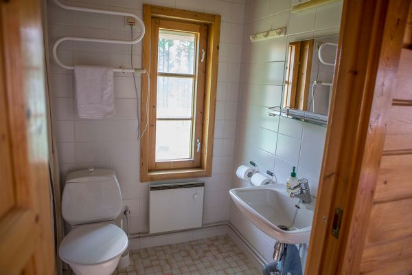 Mökkinäkymä kylpyhuoneesta jossa suihku, käsienpesuallas ja wc-istuin. 