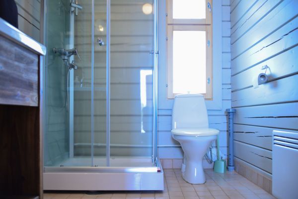 Mökkinäkymä kylpyhuoneesta jossa uusitut, vaaleast seinäpinnat, suihkukaappi ja wc-istuin.  